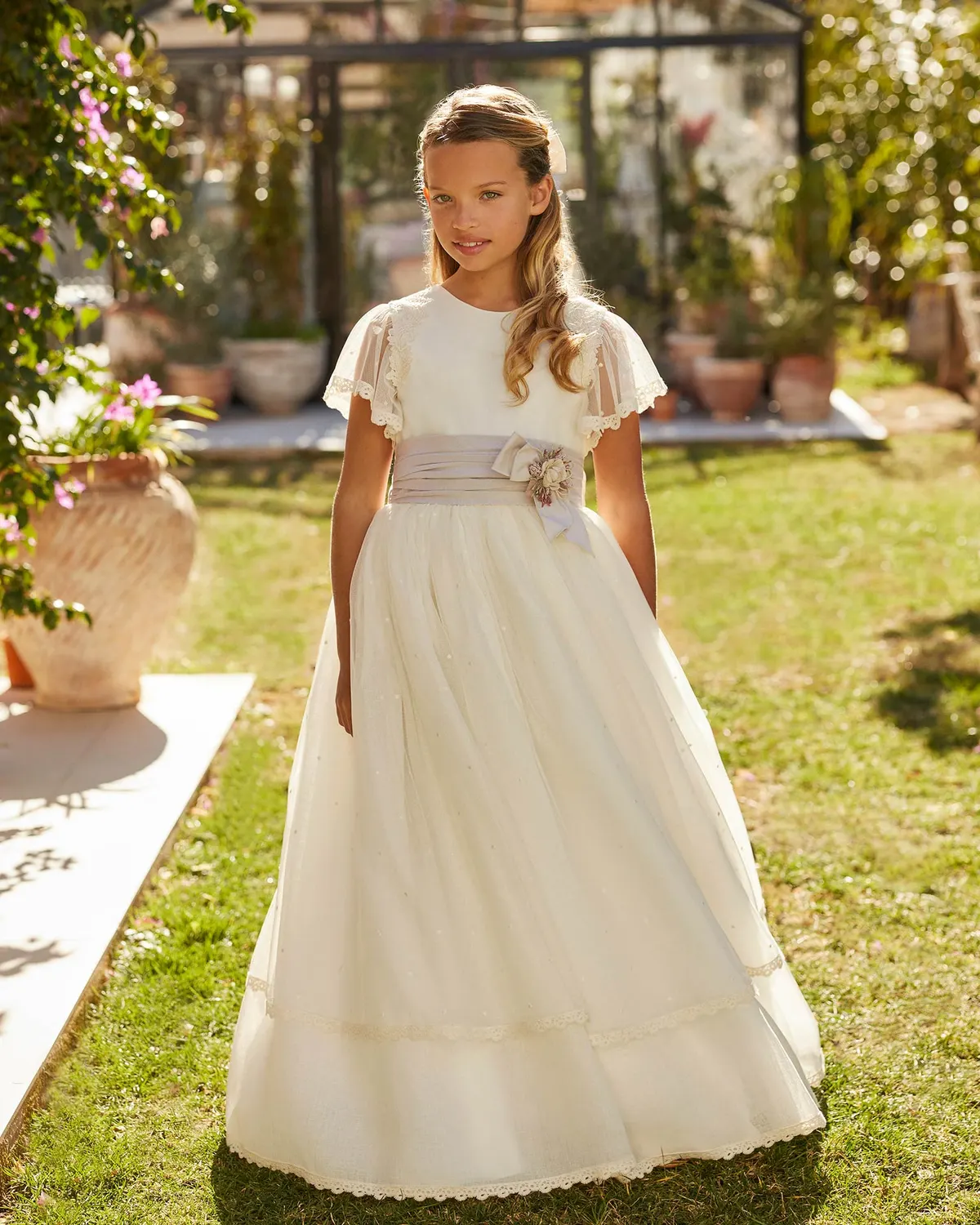 Vestido de comunión Rosa Clará First R702 de frente: mangas de tul, fajín gris malva con flores y falda de bodoques