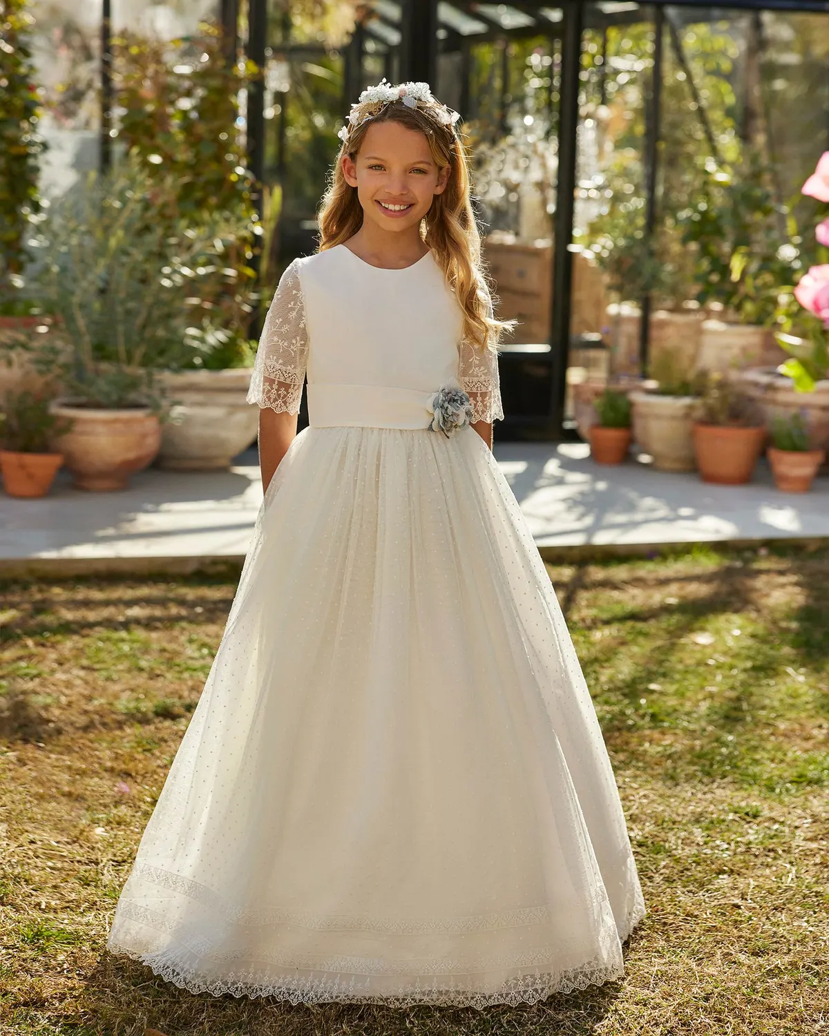 Vestido de comunión Rosa Clará First R711 de frente: mangas al codo de tul bordado, flor azul y falda de bodoques