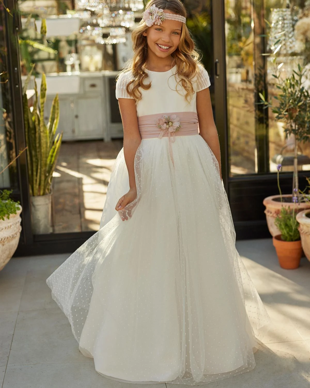 Vestido de comunión Rosa Clará First R721 de frente: cuerpo liso, fajín rosa con flores y falda de tul plumeti